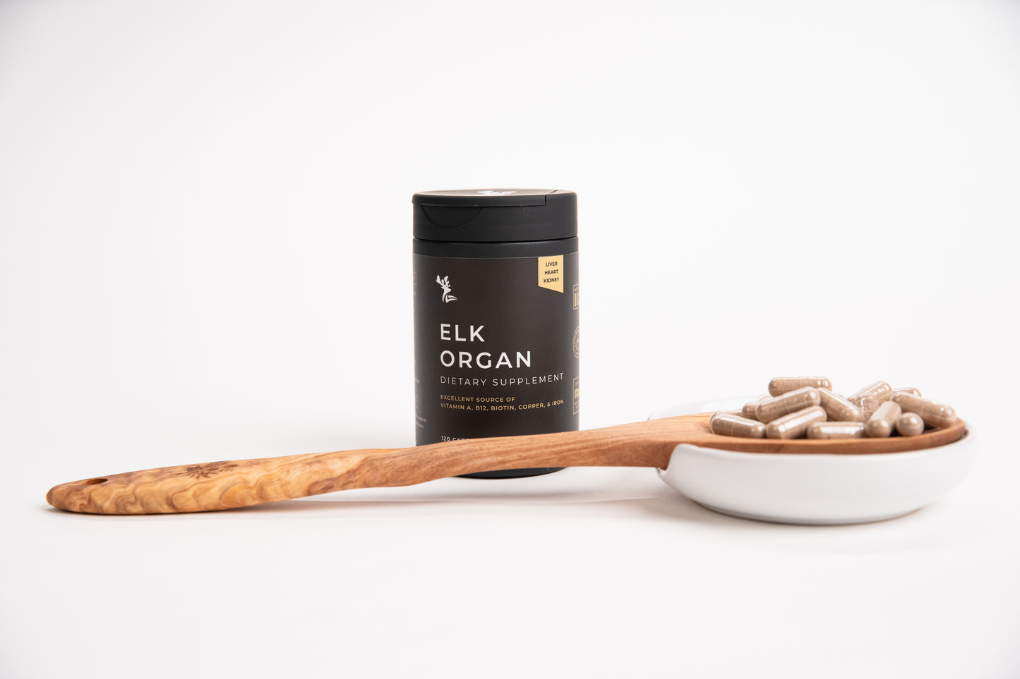 Elk Organ dietary supplement container with wooden spoon holding supplement capsules on a white background