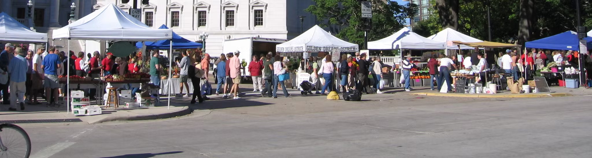 Street market with vendors under white tents on a city street.