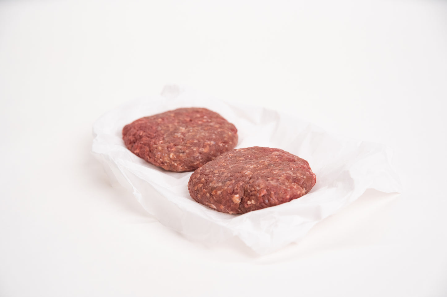 Two raw elk burger patties on a white background
