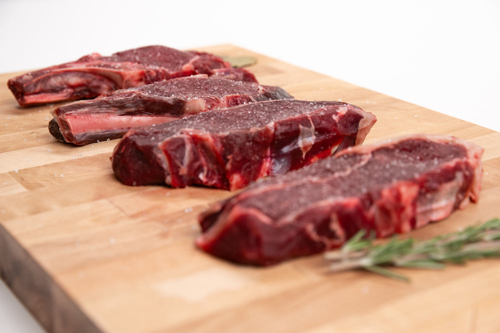 Raw elk steaks on a wooden cutting board with rosemary sprigs