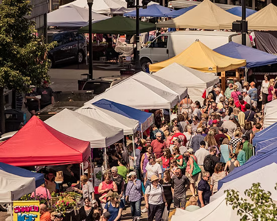 Crowded outdoor market with colorful tents and people shopping.