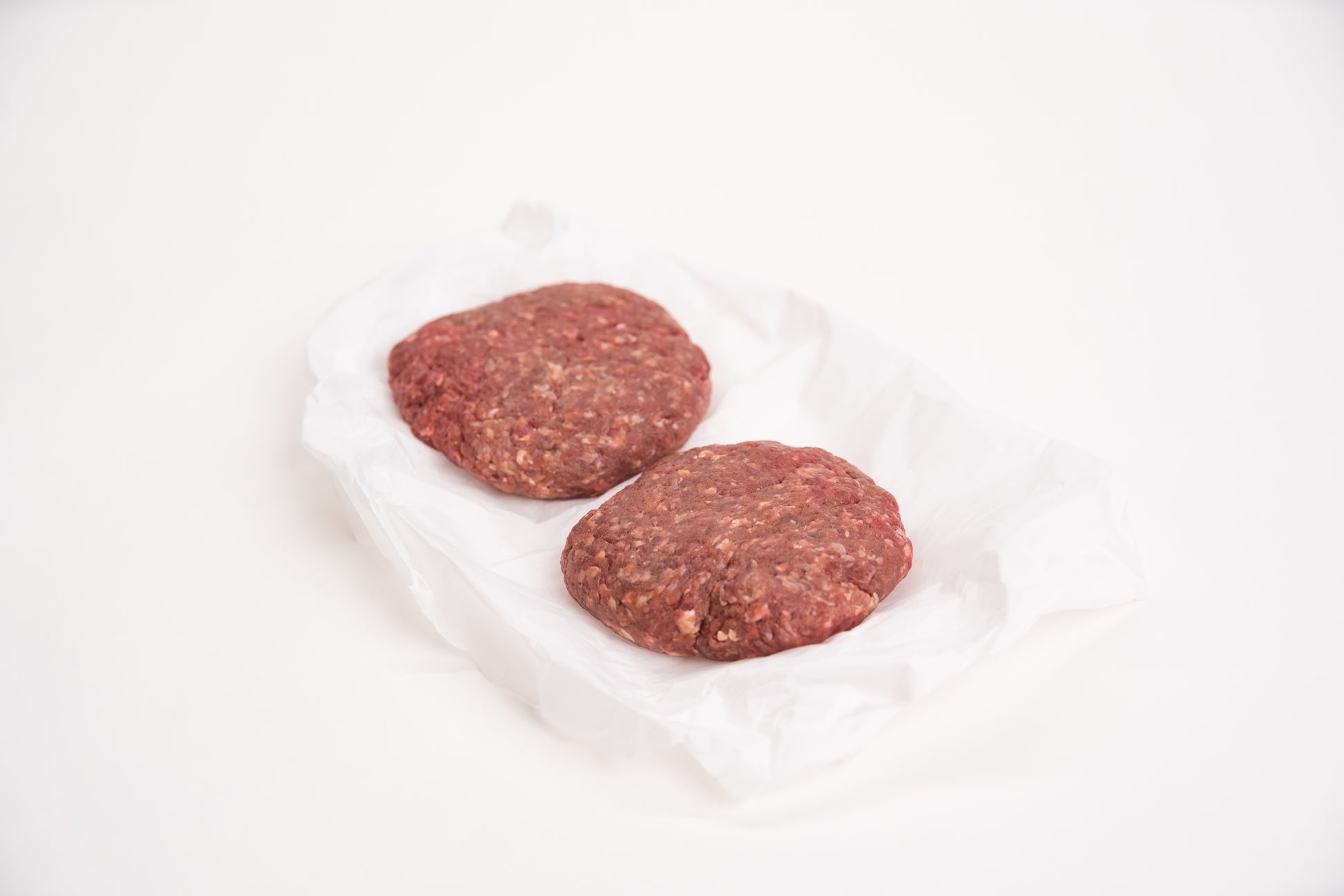 Two raw elk burger patties on a white background